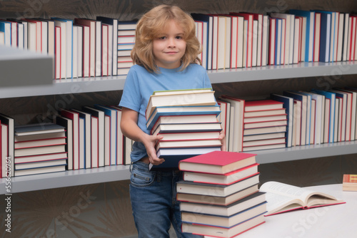 School boy with stack of books in library. School child student learning in class, study english language at school. Elementary school child. Portrait of funny pupil learning.