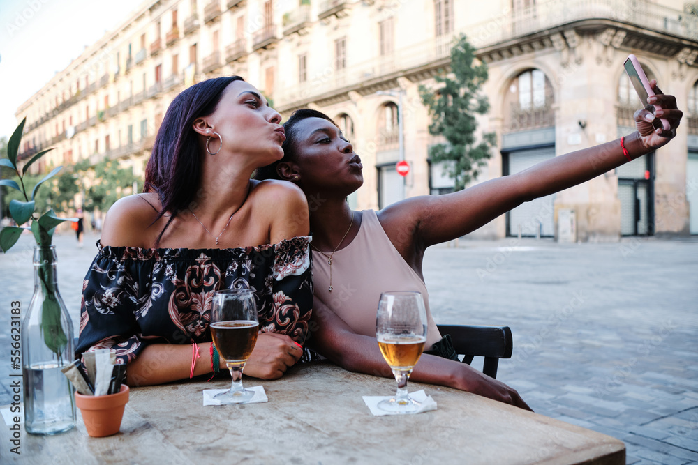 Women kissing at the camera while taking a selfie outdoors