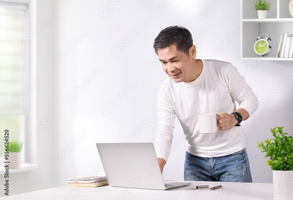 Asian holding coffee cup and touch laptop on table. Work from home conceptual.