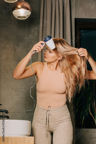Blond woman using hair dryer in bathroom at home