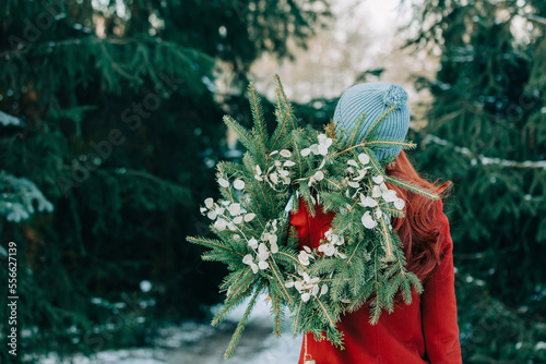 Woman wearing knit hat holding wreath in front of trees