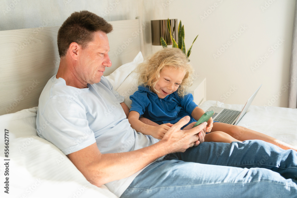 Father sharing mobile phone with daughter on bed in bedroom
