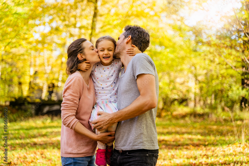 Parents with eyes closed kissing daughter in park Parents with eyes closed kissing daughter in park