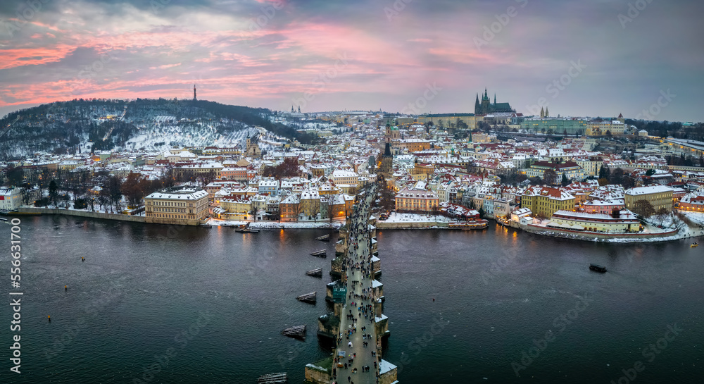 Panoramic aerial view of the snow covered cityscape of Prague, Czech Republic, with Charles Bridge and the old town during winter sunset time