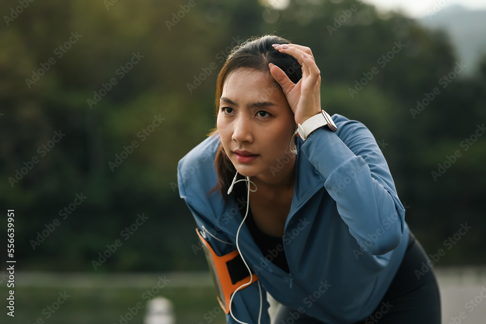 Naklejka premium Tired sportswoman wiping sweat, taking a break after running outdoors. Fitness, sport and healthy lifestyle concept