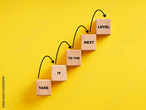 Business career path for growth and success concept. Wooden block ladder with the message take it to the next level with stepping up arrows.