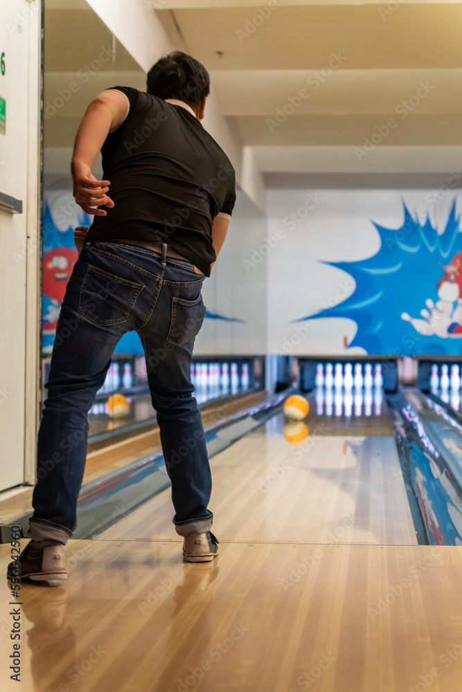 Fototapeta premium Young man playing bowling in the game area, young man throwing rolling bowling ball to target