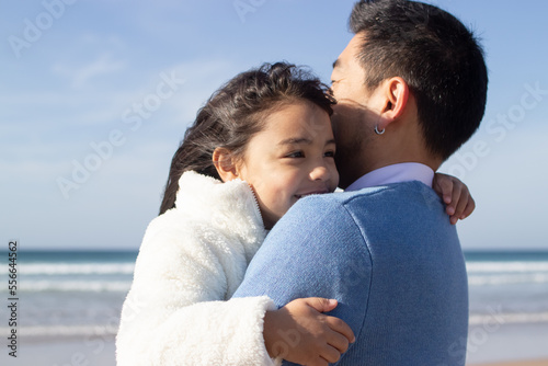 Cropped image of happy father and daughter on beach. Japanese family walking, hugging, dad carrying little girl. Leisure, family time, parenting concept © KAMPUS