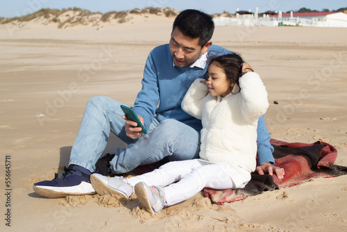 Japanese father and daughter taking selfie at beach. Dark-haired child and man holding phone and taking pictures with it. Family, technology concept
