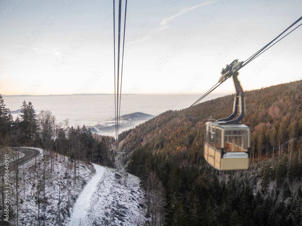 Going down a cable car with panoramic winter scene landscape above the clouds. Schauinslandbahn cabins in Freiburg, Germany. Ropeway panorama descent with snow mountain peaks and valley.