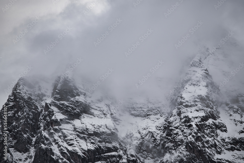 Dreamy mysterious winter landscape with fog and snow covered mountains and clouds in the sky
