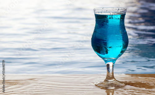 summer blue lagoon cocktail on edge of swimming pool blue color refreshing drink waterfall in background.summer vacation hotel resort bright high quality photo.scale stairs from pool