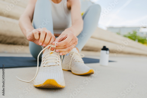 Young sportswoman tying her shoelaces while doing workout at embankment