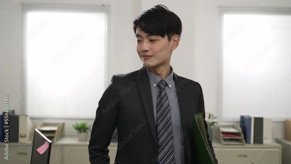 closeup view of cheerful asian male leader moving toward camera with a document and overlooking his team working hard in the office. successful leadership concept closeup view of cheerful asian male leader moving toward camera with a document and overlooking his team working hard in the office. successful leadership concept