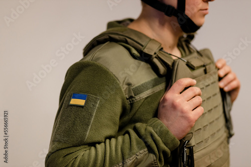  Armed Forces of Ukraine. Ukrainian soldier stands and holds hands on body armor. Ukrainian army. Ukrainian flag on military uniform. photo