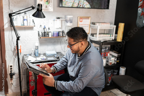 A tattoo artist is checking out his designs on his work tablet in his studio
