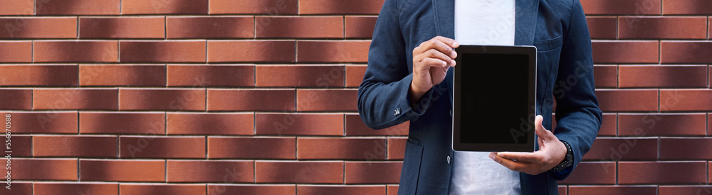Promotion. Young guy standing on wall showing screen of digital tablet looking camera smiling happy Promotion. Young guy standing on wall showing screen of digital tablet looking camera smiling happy