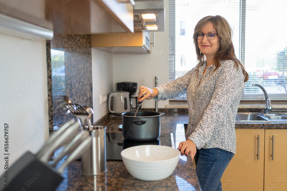 Mature white woman cooking at home and looking at the camera with a happy and smiling attitude. Mature white woman cooking at home and looking at the camera with a happy and smiling attitude.