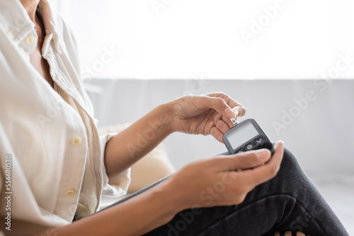 Cropped view of african american woman with diabetes using blurred glucometer at home
