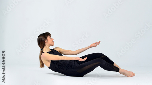 Young sporty yogi woman practicing yoga, doing Wild Thing, pose, working out, wearing sportswear, black pants and top, indoor full length, white yoga studio 