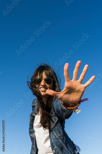 Low angle view of a similing woman while showing the palm of her hand. Blue sky background. Copy space. Stop gesture.
