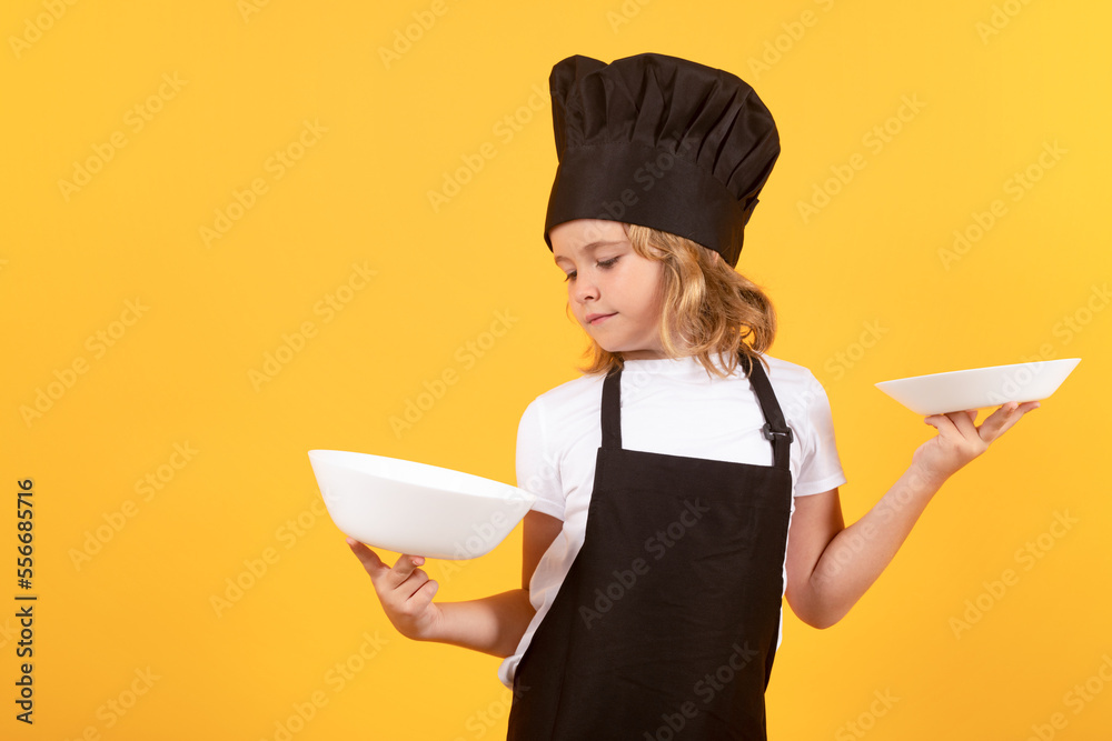 Little cook with cooking plate. Kid in cooker uniform and chef hat preparing food on studio color background. Cooking, culinary and kids food concept.