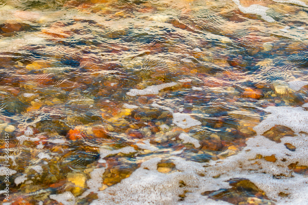 Multi-colored sea stones under transparent water. Crystal clear waves and pebbles.