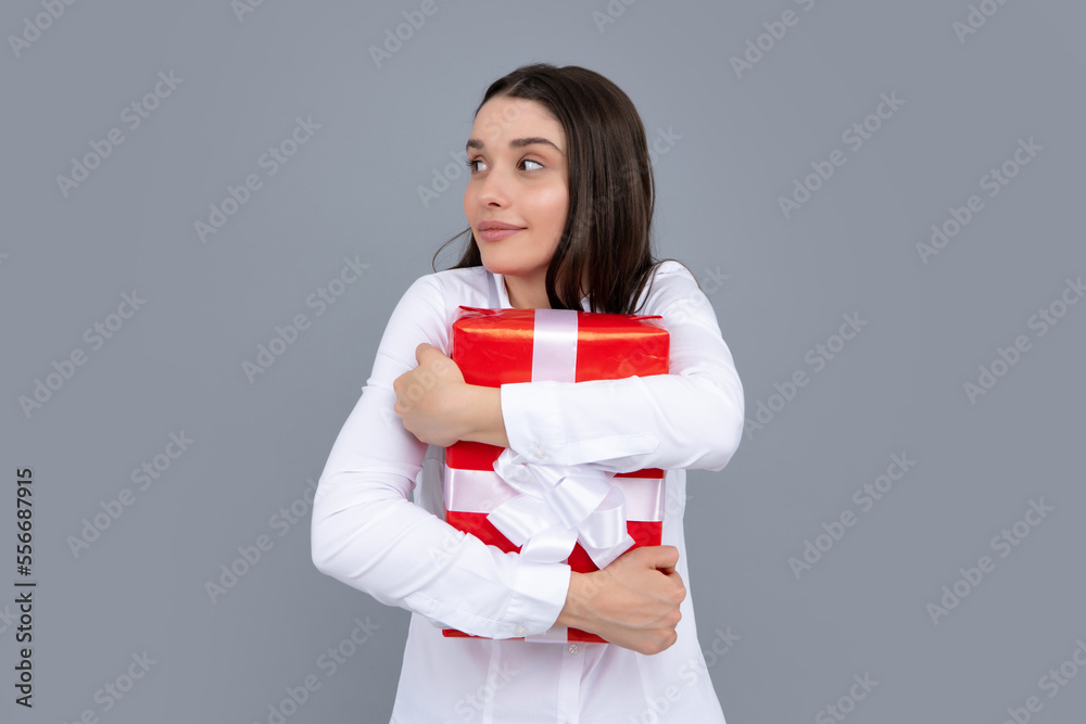 Surprised woman holding gift. Smiling beautiful young brunette woman in shirt hold present box with gift ribbon bow isolated on bright gray background, studio portrait. Birthday concept. Surprised woman holding gift. Smiling beautiful young brunette woman in shirt hold present box with gift ribbon bow isolated on bright gray background, studio portrait. Birthday concept.