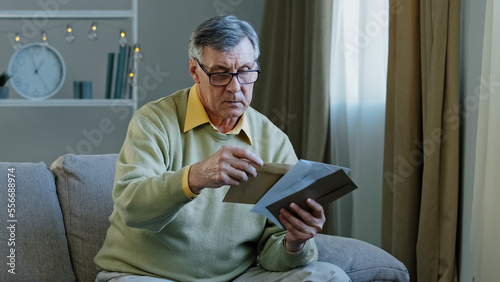 Fotografía 60s elderly man recipient with glasses sorting letters in living room concentrat