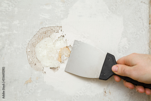 Young adult man hand using spatula and plastering concrete wall hole with putty on mesh. Closeup. Repair work of home. Renovation process.