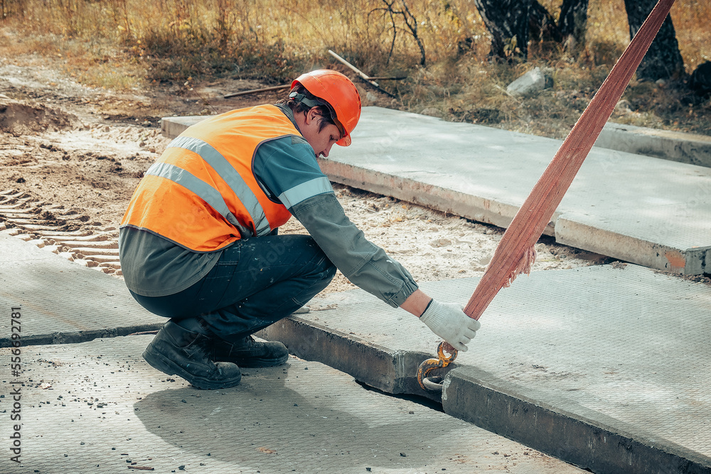 Slinger lays concrete slab on construction site on summer day. Worker