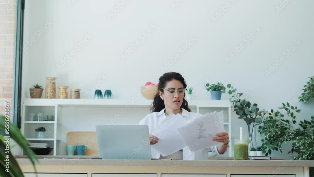 Video of  worried woman tossing invoices and documents into the air while working on the laptop at home.