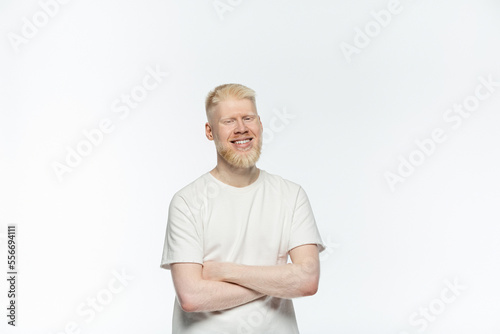 bearded albino man in t-shirt smiling and standing with crossed arms isolated on white