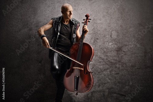 Punk musician leaning on a gray rugged wall and playing a cello