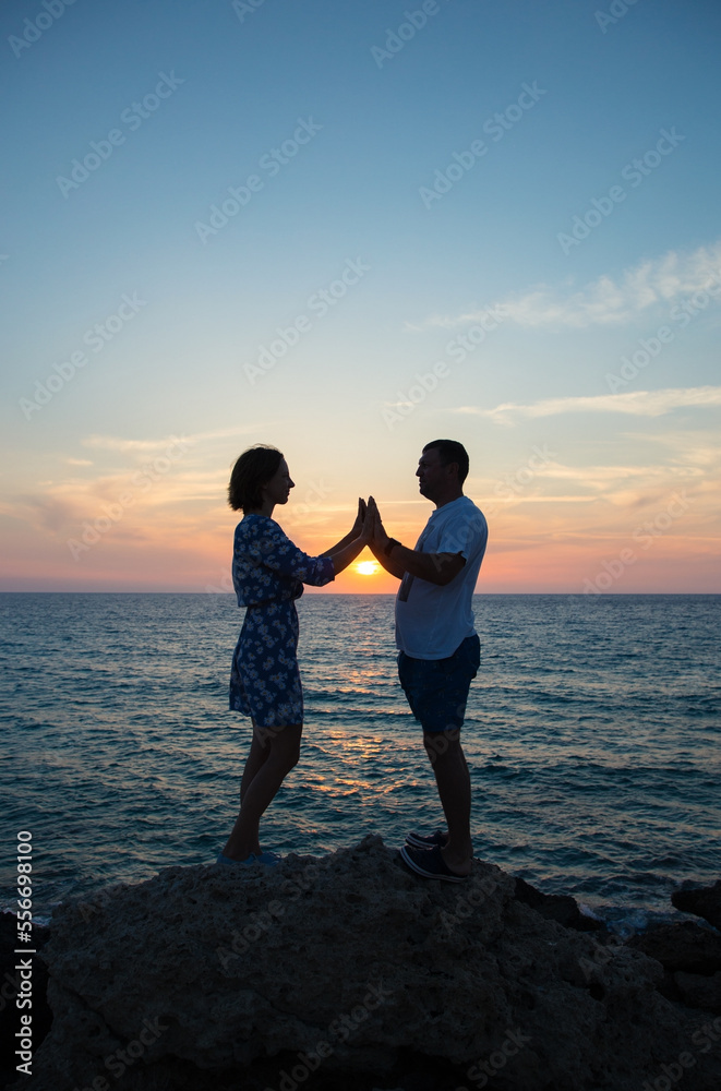 full-length silhouettes of couple in love, against backdrop of sea and sunset, stand opposite each other. holding hands. enjoyment of moment, tender feelings, pleasant pastime. Valentine's Day