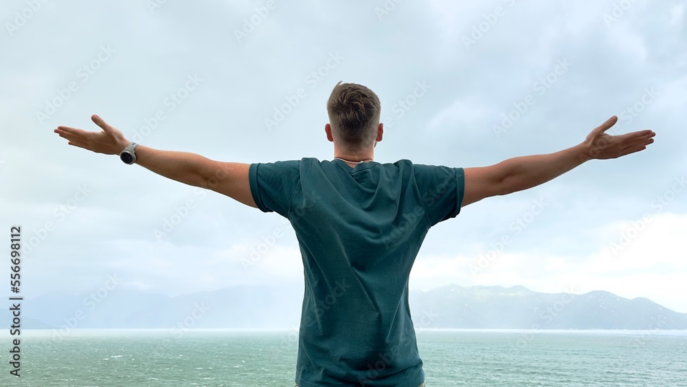 happy handsome free guy, young calm relaxed carefree man traveler with open raised hands enjoy sea, ocean view, person feeling good, breath deep deeply fresh air. Freedom, travel, happiness concept