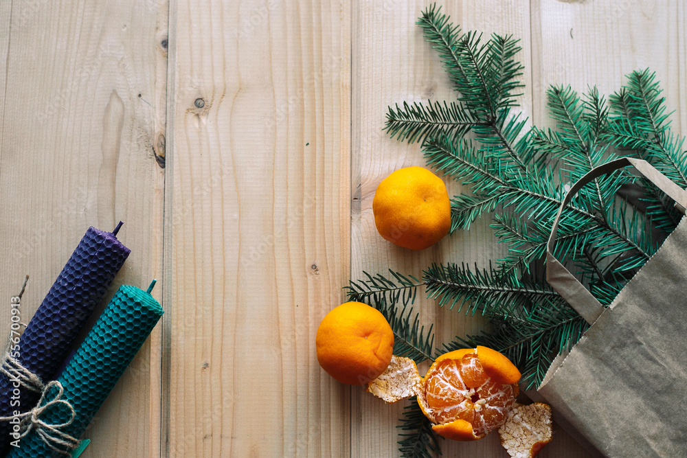 Branches of a Christmas tree that are visible from a paper gift bag, tangerines, two candles on a light wooden background, top view, a place to copy Branches of a Christmas tree that are visible from a paper gift bag, tangerines, two candles on a light wooden background, top view, a place to copy