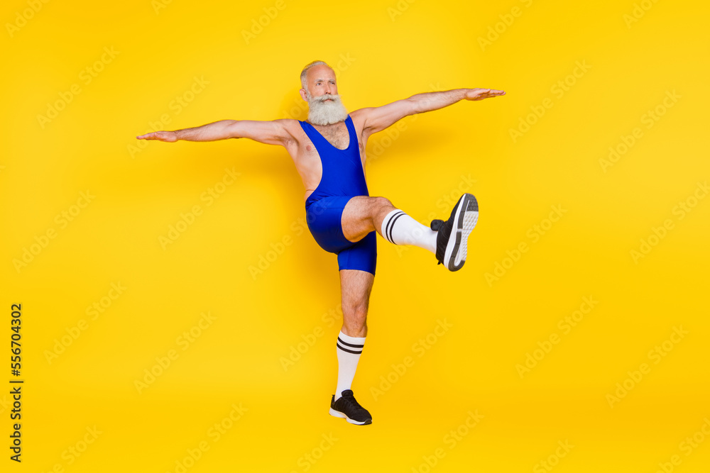 Full length photo of sporty muscular motivated senior man doing morning exercises raise hand legs isolated on yellow color background