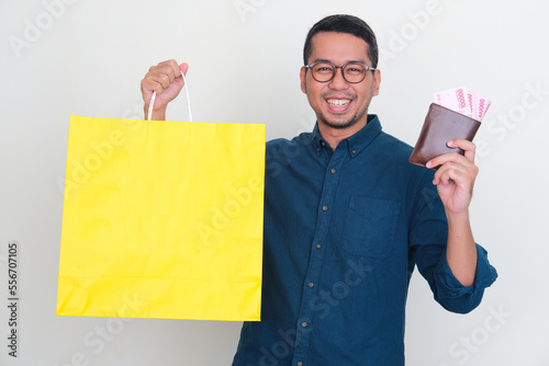 Asian man smiling happy while holding yellow shopping bag and wallet full of money photo