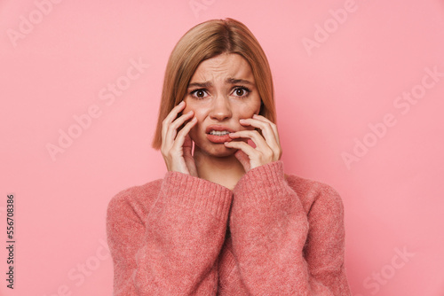 Disgusted young girl touching her face and looking at camera isolated over pink background