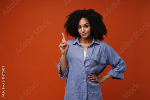 Young afro woman pointing finger away at copy space isolated