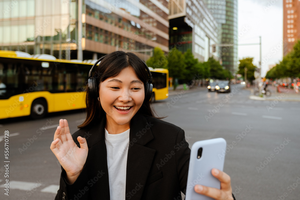 Fototapeta premium Young woman using cellphone and headphones while walking on street