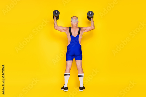 Full body rear portrait of sportive aged person hands lifting dumbbells isolated on yellow color background