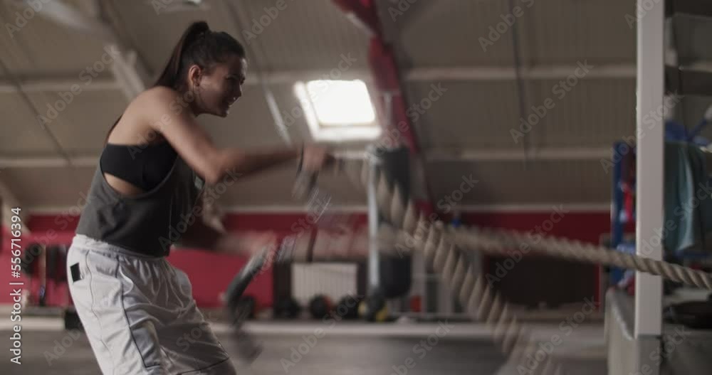 Aggressive female boxer exercising with battle ropes