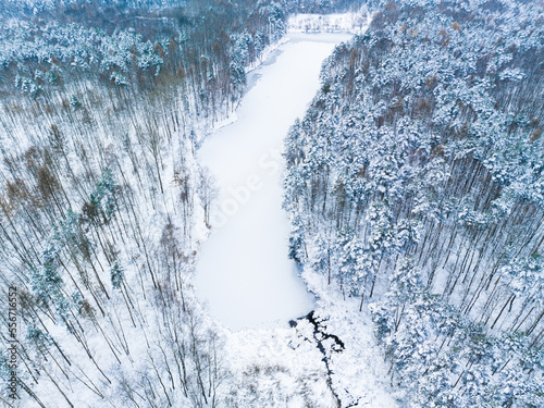 Aerial view of a frozen lake, a pond in the middle of the forest. The concept of a winter landscape, a beautiful view of a winter forest and a pond recorded from a drone.