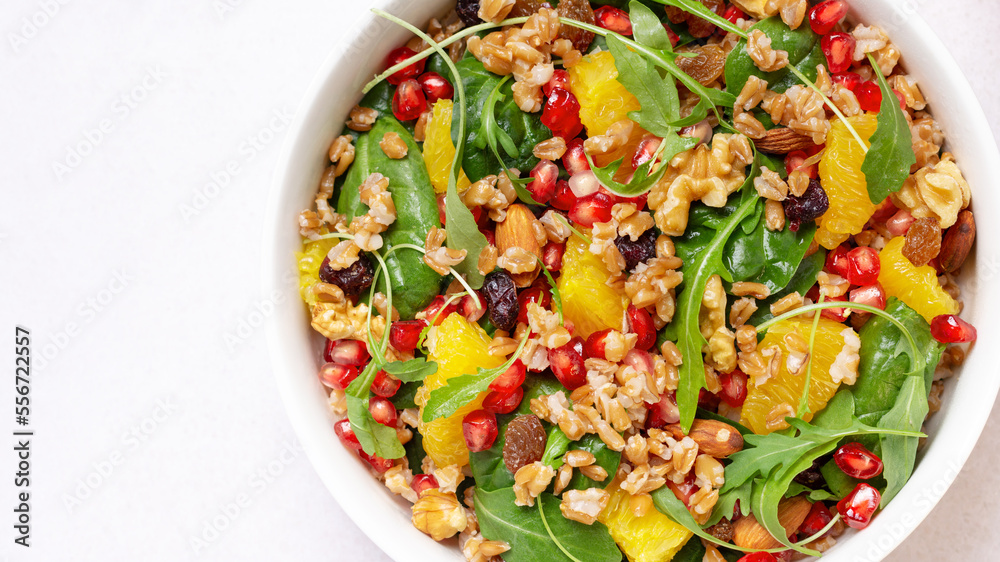 Healthy salad with spelt, oranges, pomegranate seeds. greens and nuts on light background, minimal style