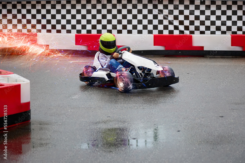 Child driving a real go-kart on a children's race track carefully bypasses an obstacle. Young karting racer trains at the circuit on wet asphalt after the rain