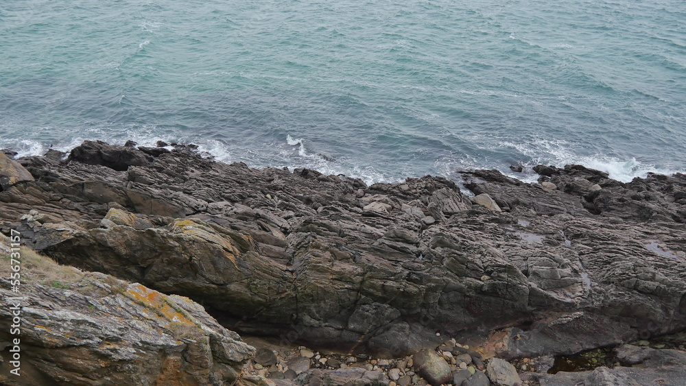 Falaises près d'une mer agité, sous un ciel nuagueux, gris et menaçant, eau fracassant contre les rochers, falaises en roches et de la verdure et végétation, côté bretonne, coin de la Bretagne
