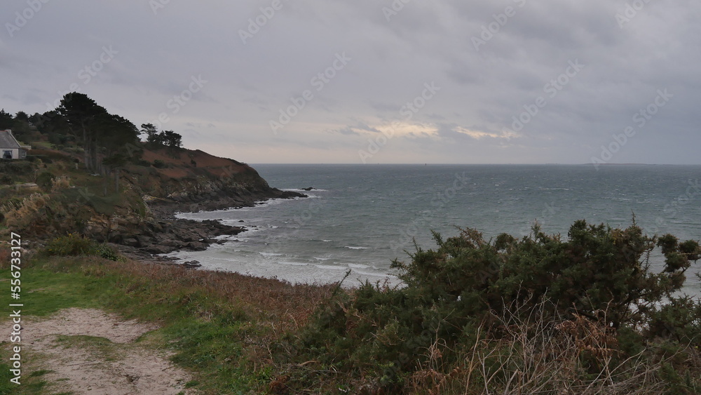 Falaises près d'une mer agité, sous un ciel nuagueux, gris et menaçant, eau fracassant contre les rochers, falaises en roches et de la verdure et végétation, côté bretonne, coin de la Bretagne