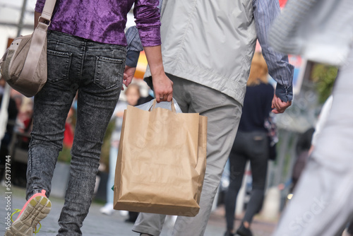 Junge Frau und älterer Herr sowie weitere Personen beim Shopping in einer Einkaufsstraße oder Fußgängerzone mit Einkaufstüten, selektiver Fokus © redaktion93